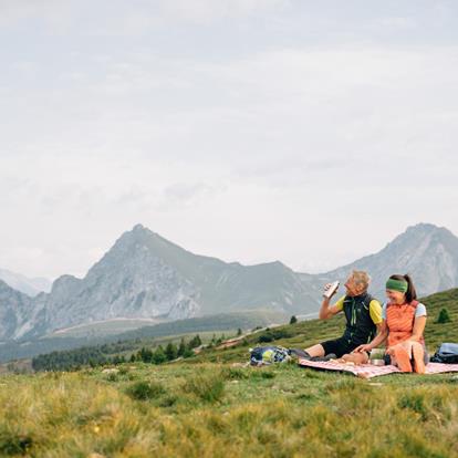 Mann und Frau im Sommer auf einer Almwiese auf Picknickdecke mit Hintergrund Berg Ifinger in Hafling in Südtirol.