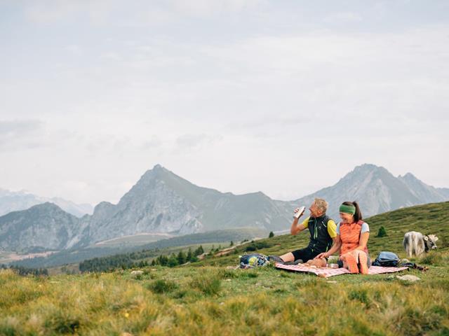 Mann und Frau im Sommer auf einer Almwiese auf Picknickdecke mit Hintergrund Berg Ifinger in Hafling in Südtirol.