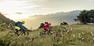 Two people ride on their downhill bike from the mountain to the valley.