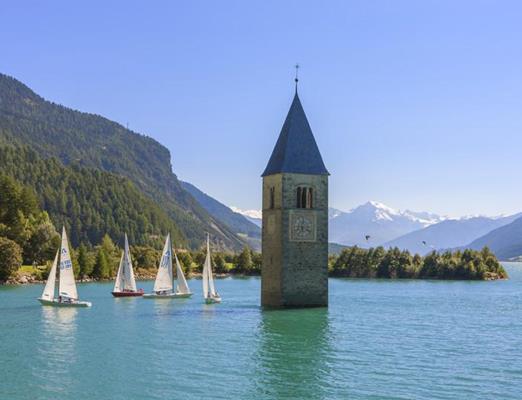 Reschensee mit versunkenem Glockenturm, umgeben von Segelbooten